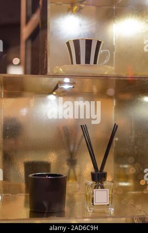 Aromatic reed diffuser air freshener and candle on golden mirror shelf at spa interior. Stock Photo