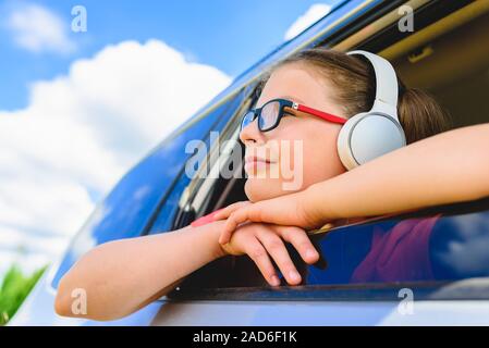 Cute girl listening to music with headphones - looking through open window of the car Stock Photo