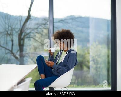 black woman drinking coffee and using a mobile phone  at home Stock Photo