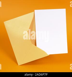 Metallic gold envelope with blank message card letter or invitation isolated on an orange background.  Space for copy. Stock Photo