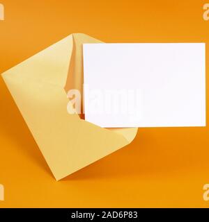 Metallic gold envelope with blank message card letter or invitation isolated on an orange background.  Space for copy. Stock Photo