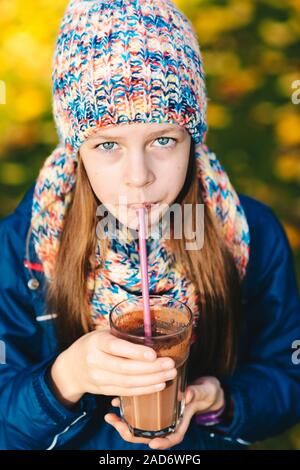 Young girl drinking chocolate milkshake drink in autumn park Stock Photo