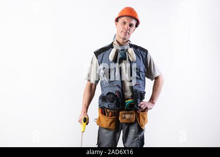 The builder in a helmet, and unloading, holds a hacksaw in his hands on a tree. On a light background. Stock Photo