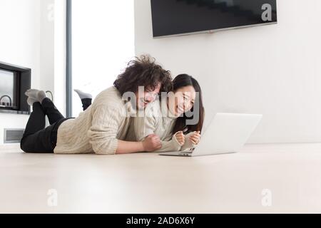 young multiethnic couple using a laptop on the floor Stock Photo