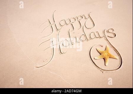Tropical Happy Holidays message handwritten in calligraphy script with natural starfish on smooth sand beach Stock Photo