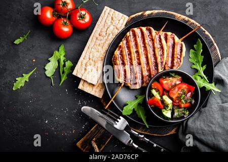 Juicy grilled chicken meat lula kebab on skewers with fresh vegetable salad on black background, top view Stock Photo