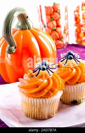 homemade halloween cupcakes decorated with toy plastic spiders and other desserts are in the background. Stock Photo