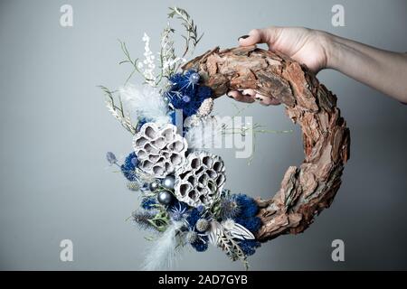 Close-up of a florist's hand holding a Christmas wreath with fir branches and cones on the table. Stock Photo