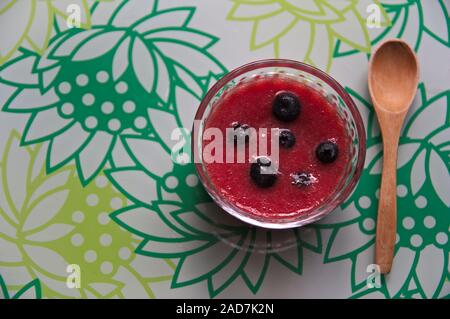 Flat lay of a decorated surface on which we see a bowl with strawberry juice with blueberries, a wooden spoon and space on the left Stock Photo