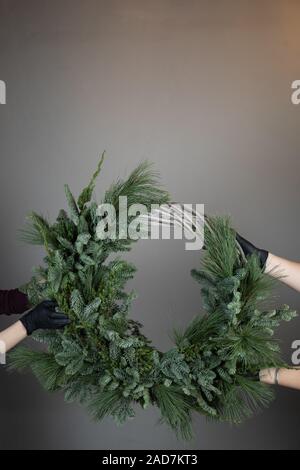 Close-up of a florist's hand holding a Christmas wreath with fir branches and cones on the table. Stock Photo