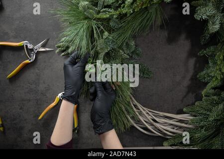 Top view of florist hands making Christmas wreath with fir branches on the table Stock Photo