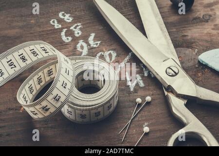 Tailoring scissors, measuring tape, thimble, including pins, chalk. Human body measurements are written on a wooden board. Stock Photo