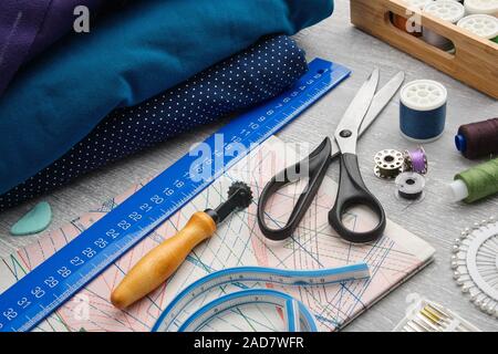 Sewing items: tailoring scissors, measuring tape, spools of thread, patterns on paper, seamstress cutting knife, sewing layout, rulers, including pins Stock Photo
