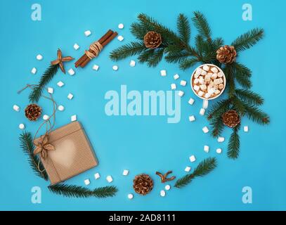 Trendy Christmas background of hot chocolate with marshmallow, ginger cookies, craft gift box, Christmas tree branches with golden cones on cyan blue Stock Photo