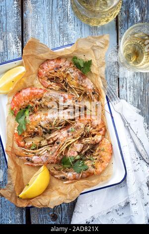 Traditional fried black tiger prawn with lemon and white wine as top view in a white casserole on a wooden blue board Stock Photo