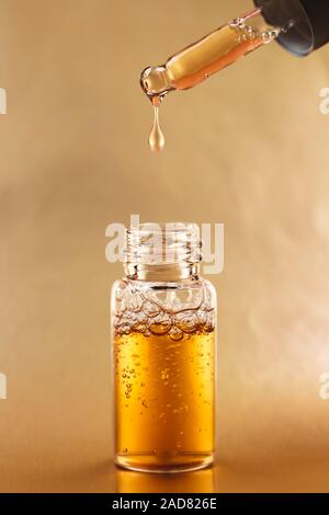 Bottle of cosmetic oil with pipette on golden background. Front view. Stock Photo