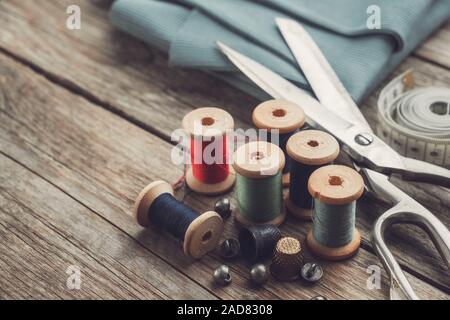Retro sewing items: tailoring scissors, thimbles, buttons, wooden thread spools, measuring tape and green fabric. Stock Photo