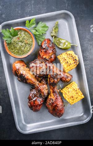 Traditional barbecue chicken drumsticks with corn and chimichurri sauce as top view in a silber fryer Stock Photo