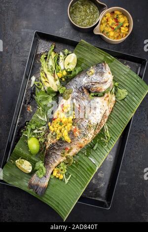 Fresh barbecue gilthead seabream with lettuce and mango chutney as top view on a green banana leaf Stock Photo