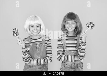 Anime cosplay party concept. Happy little girls. Anime fan. Kids with artificial hairstyles eating lollipops. Anime convention. Vibrant characters fantastical themes. Modern childhood. Childrens day. Stock Photo