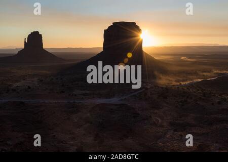 Sunrise flares behind the buttes in Monument Valley, Arizona, US
