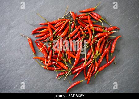 A pile of bright red Thai bird chiles on a black slate background; view from above Stock Photo