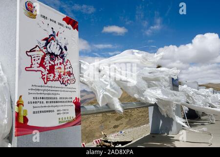 White silk scarves blow wildly next to a sign asserting Chinese government control over the people of Tibetan Plateau. Stock Photo