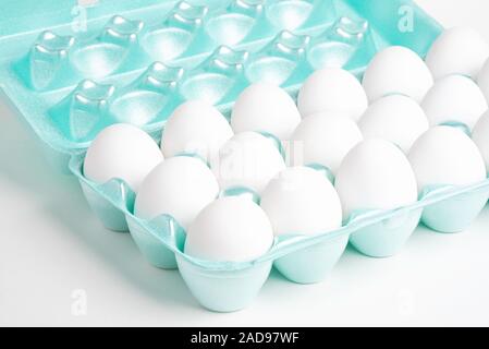 A close-up shot of a bright green styrofoam crate full of white eggs set on a white background. Stock Photo