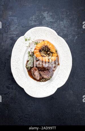 Traditional German braised pork cheeks in brown red wine sauce with mushroom and pumpkin as top view on a shabby chic design whi Stock Photo