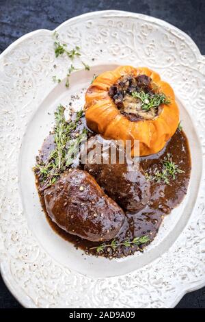 Traditional German braised pork cheeks in brown red wine sauce with mushroom and pumpkin as closeup on a shabby chic design whit Stock Photo