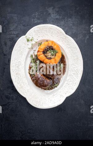 Traditional German braised pork cheeks in brown red wine sauce with mushroom and pumpkin as top view on a shabby chic design whi Stock Photo