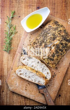 Traditional Italian ciabatta bread with herbs and olive oil as top view on a cutting board
