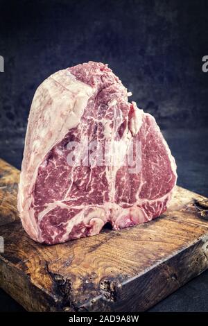 Traditional raw dry aged wagyu porterhouse steak as closeup on an old rustic board - vintage Stock Photo