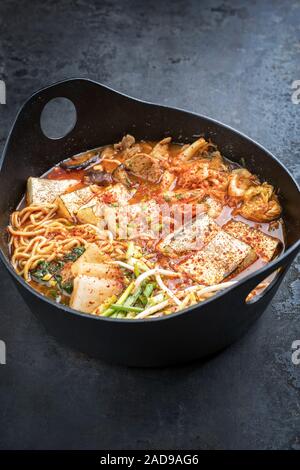 Traditional Korean kimchi jjigae with grilled pork belly and ramen as closeup in a modern design Japanese cast-iron roasting dis Stock Photo