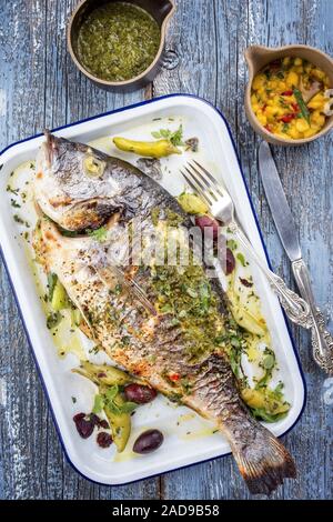 Fresh barbecue gilthead seabream with mango chutney and chimichurri as top view in a white skillet Stock Photo