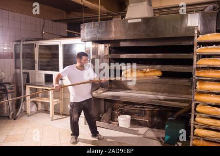 bakery worker taking out freshly baked breads Stock Photo