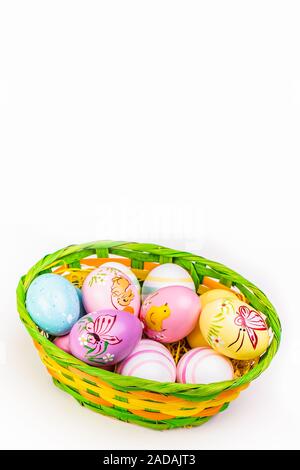 Wicker basket with Easter eggs hand painted on white tabletop background Stock Photo