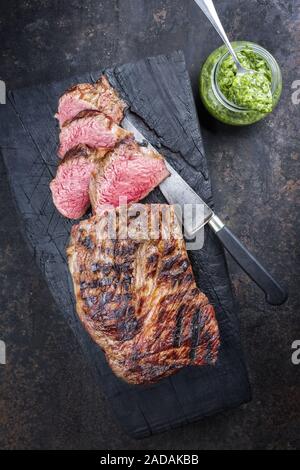 Barbecue Argentinian dry aged wagyu tri tip steak with chimichurri sauce as dip as top view on a carbonized wooden board Stock Photo