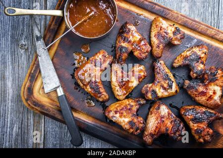 Traditional barbecue chicken wings with hot chili sauce as top view on a burnt cutting board Stock Photo
