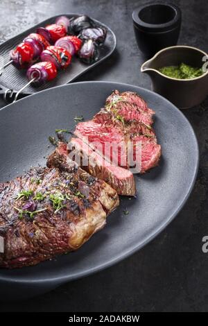 Barbecue dry aged wagyu tri tip steak sliced with hot sauce and tomato onion skewer as closeup on a modern design cast iron plat Stock Photo