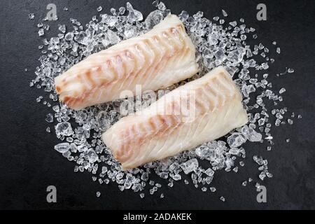 Raw Norwegian skrei cod fish filet as top view on crashed ice on a black board with copy space Stock Photo