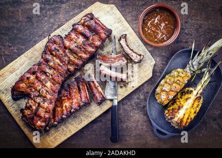 Barbecue spare ribs St Louis cut with hot honey chili marinade and pineapple as top view on a rustic cutting board with copy spa Stock Photo