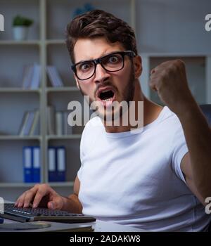 Young man staying late in office to do overtime work Stock Photo