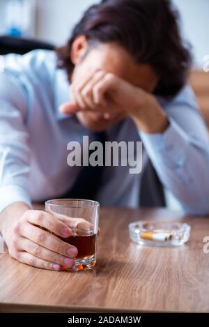 Male employee drinking alcohol and smoking cigarettes at workpla Stock Photo