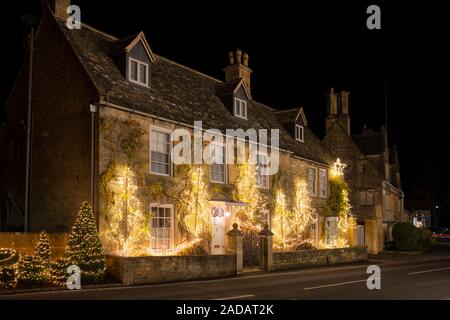 Christmas tree light decorations on the front of a house and in the trees in Broadway at night. Broadway, Cotswolds, Worcestershire, England Stock Photo