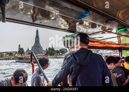 Bangkok, Thailand - November 17, 2019: Passengers in river taxi on Chao Phraya river go past Wat Arun (Temple of Dawn) in the capital of Thailand