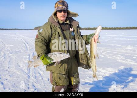 man of Caucasian appearance with a beard holds a large fish pike trophy. Winter fishing winter sport Stock Photo