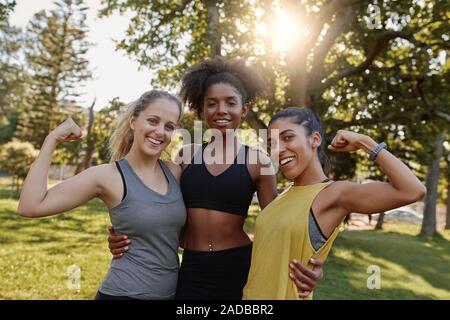 Portrait of an african american female woman standing with her two diverse friends flexing their muscle in the park - 3 woman showing strength and Stock Photo