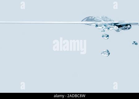 Side view of a waterline with rising bubbles against light blue background. Stock Photo