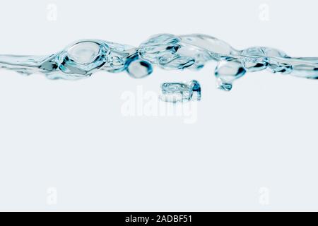 Studio shot of a row of moving bubbles at the water surface in front of bright blue background. Stock Photo
